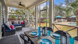 A covered patio with wicker furniture, a table set for dining, and a view of a backyard with a pool and patio furniture. - Spacious Retreat with Private Pool, Outdoor Oasis w/Firepit & Grill, and 8 Bikes (Seacrest Beach West)