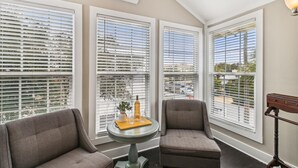 A room with three large windows, a small round table with a plant and a bottle, two grey armchairs, and a wooden floor lamp. - Spacious Retreat with Private Pool, Outdoor Oasis w/Firepit & Grill, and 8 Bikes (Seacrest Beach West)