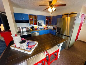 A modern kitchen with blue cabinets, stainless steel appliances, and a wooden island with a coffee station.