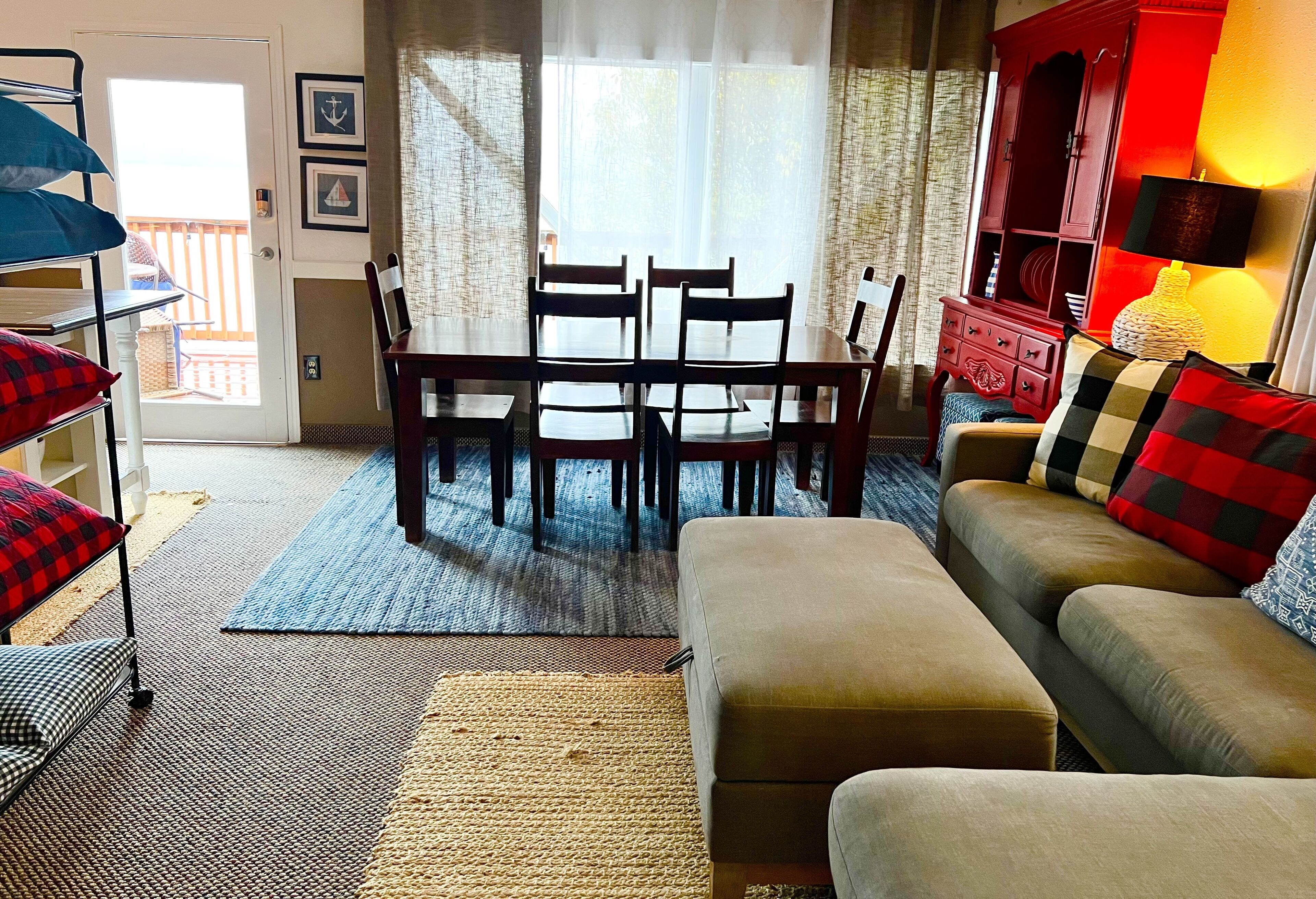 A living room with a sofa, a dining table with chairs, a red cabinet, and a view through a door to an outdoor balcony.