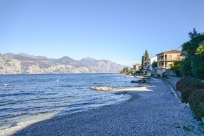 Une plage de galets bordée d’une eau d’un bleu limpide, un littoral rocheux et des bâtiments dotés de balcons donnant sur la mer.