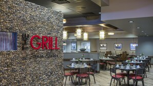 A restaurant with a stone wall and the word "GRILL" in red letters. Tables are set with red chairs and centerpieces.