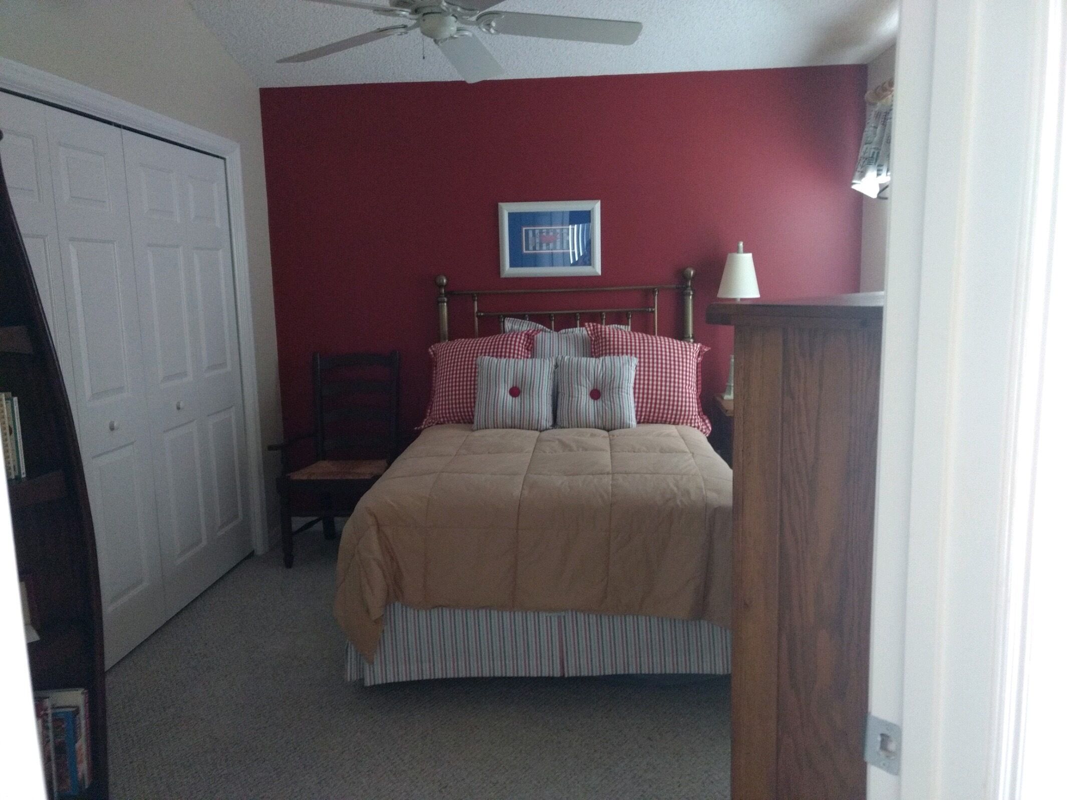 A bedroom with a bed, a chair, a ceiling fan, a door, and a framed picture on the wall.