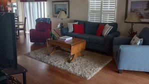 A living room with a sofa, armchairs, a coffee table, and a TV. There are framed pictures on the walls and a window with blinds. - Beautiful Villa in the Heart of Florida's Friendliest Active Adult Community (The Villages)