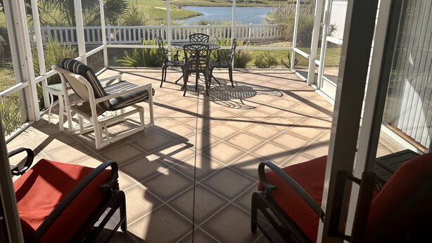 A covered patio with a view of a lake, outdoor furniture, and a white fence. - Beautiful Villa in the Heart of Florida's Friendliest Active Adult Community (The Villages)
