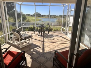 Un patio cubierto con vistas a un lago, mobiliario exterior y una valla blanca.