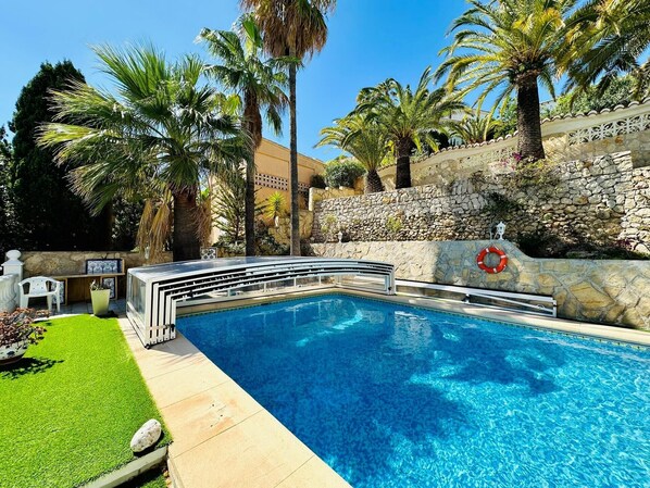 A swimming pool with a stone wall and palm trees. - Villa Camelia - Benitachell, Costa Blanca (Benitachell)