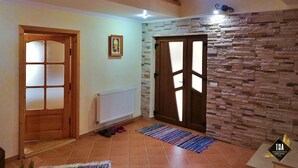 A spacious interior with a wooden staircase, a stone wall, and a door with frosted glass panels. - Casa Lacry (Manastirea Humorului)