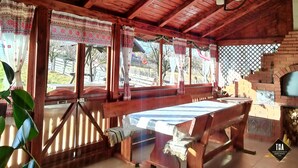 A rustic wooden room with a large table and benches, large windows with curtains, and a hanging light fixture. - Casa Lacry (Manastirea Humorului)