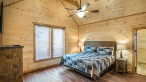 Ein Schlafzimmer einer Holzhütte mit einem Bett, zwei Fenstern mit Jalousien, einem Deckenventilator und einem Nachttisch mit Lampe.