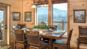 Ein Esszimmer aus Holz mit einem Tisch, der für sechs Personen gedeckt ist, umgeben von Stühlen und großen Fenstern mit Blick auf die Berge.