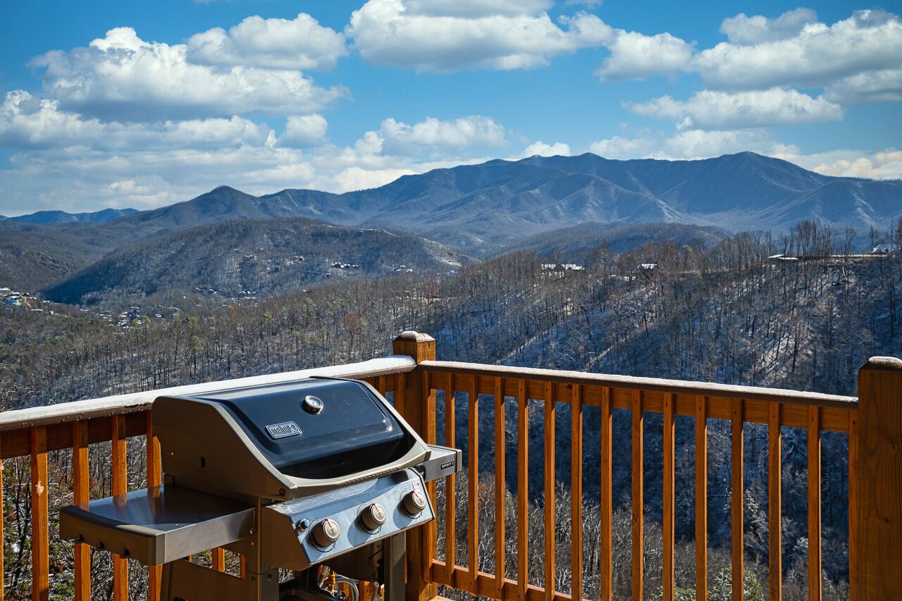 A barbecue grill on a wooden deck overlooking a mountainous landscape.