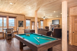 A wooden interior with a pool table, chairs, a sofa, and a fireplace.