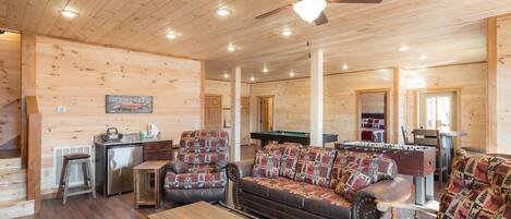 A spacious wooden cabin interior with a living room, kitchen, and a pool table.