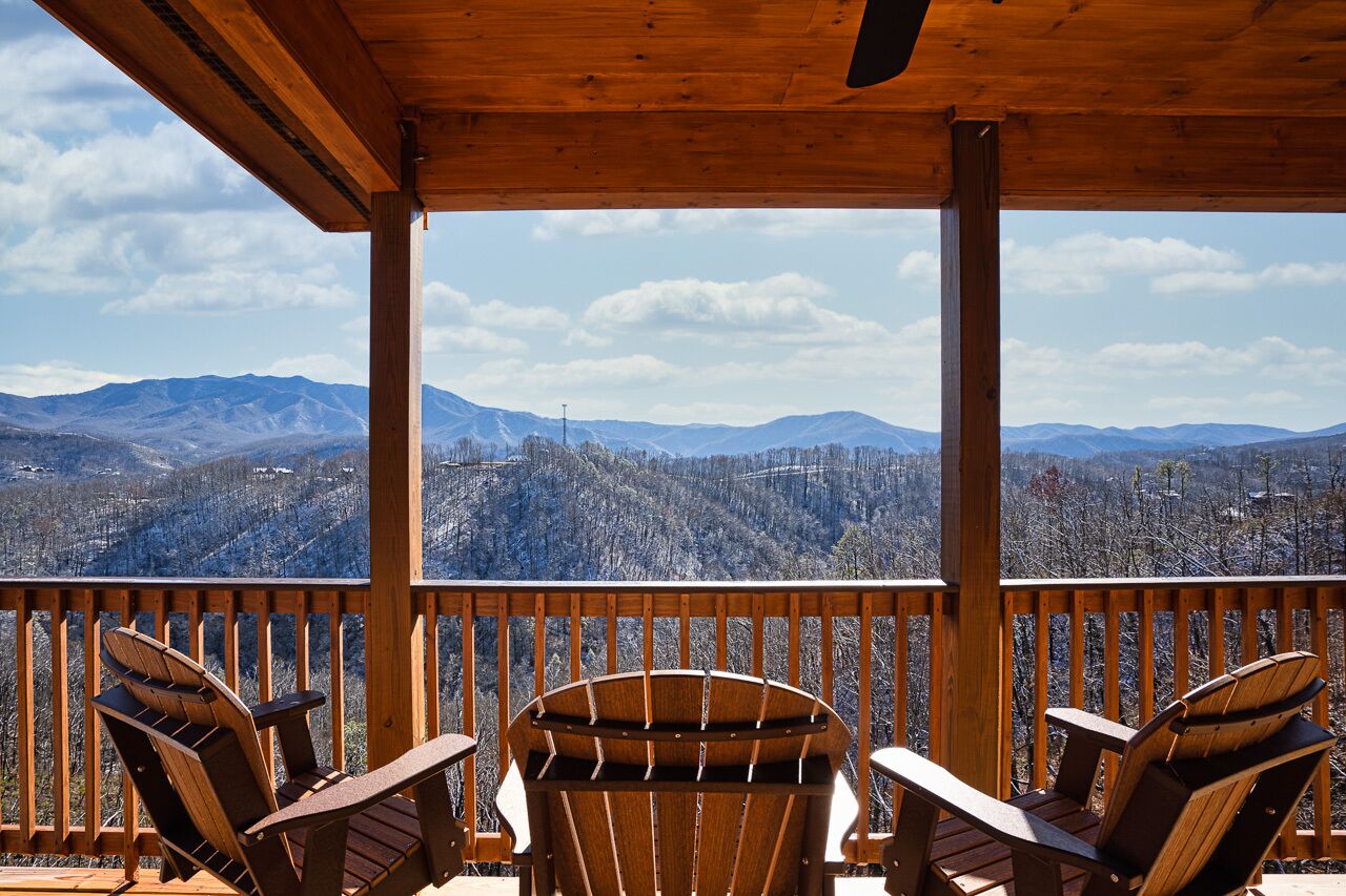 A wooden deck with Adirondack chairs overlooking a mountainous landscape.