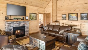 Ein gemütliches Blockhaus-Interieur mit Kamin aus Stein, Ledermöbeln und einem flachbildschirmfernseher darüber.