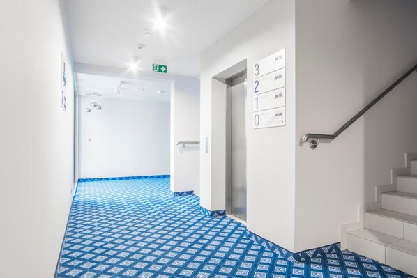 A hallway with a blue patterned floor, a staircase, and a wall with numbered signs. - Hotel Urbi (Gdansk)