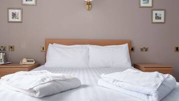 Uma cama bem arrumada com roupa de cama e toalhas brancas, cabeceira de madeira, mesas de cabeceira com uma lâmpada e um telefone, e quadros nas paredes.