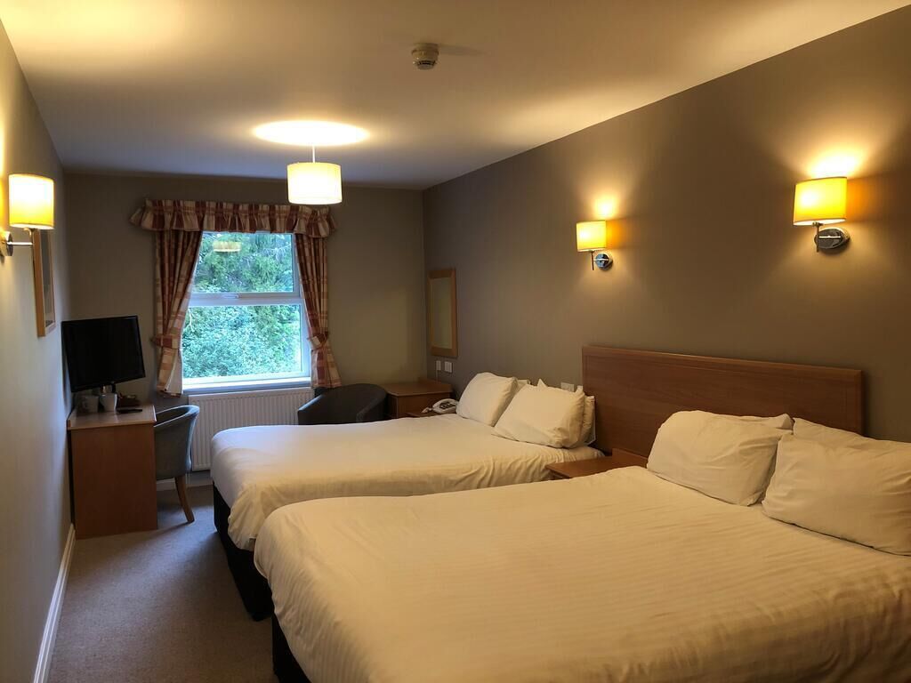 A hotel room with two beds, a desk, a chair, a TV, and a window with curtains.