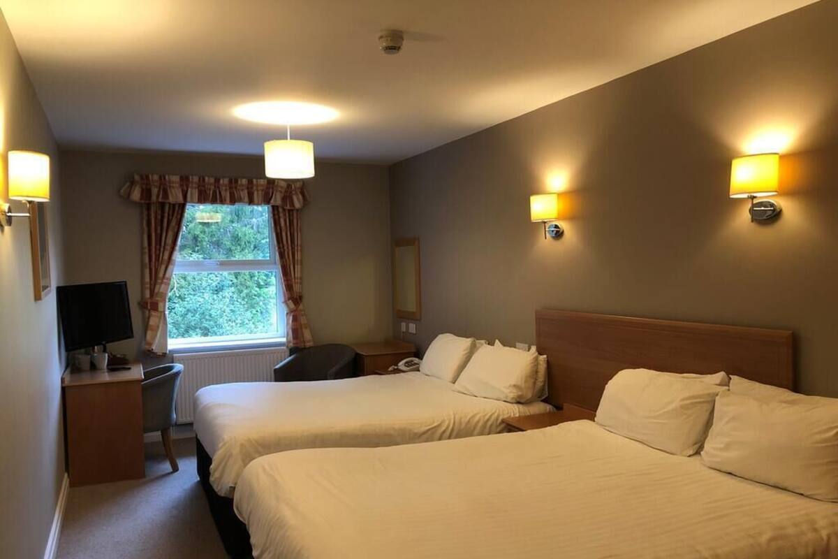 A hotel room with two beds, a desk, a chair, a TV, and a window with curtains.
