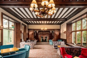 A spacious room with a fireplace, wooden beams, and large windows. - Windermere Manor (Windermere)