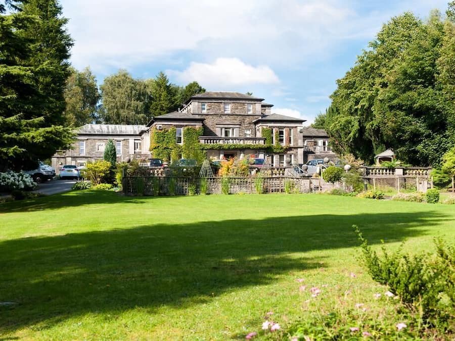 A large, historic stone building with a symmetrical facade, surrounded by a well-maintained lawn and mature trees.