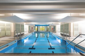 A swimming pool with clear lanes, surrounded by lockers and a view of greenery outside. - Windermere Manor Hotel (Windermere)
