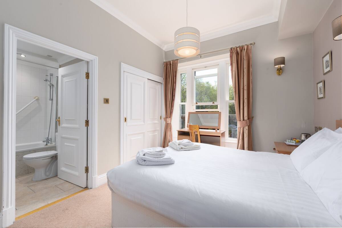 A hotel room with a large bed, a bathroom with a shower, and a view of the outdoors.
