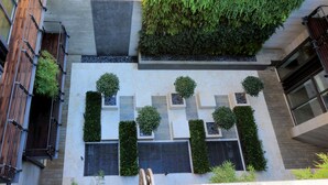Un bâtiment moderne doté d’une cour intérieure comprenant un balcon en bois, un jardin vertical et des jardinières bien disposées, où sont plantés des arbustes.