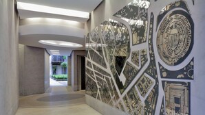 Un couloir moderne orné d’une fresque représentant un paysage urbain, doté d’un éclairage encastré et offrant une vue sur un autre espace agrémenté de plantes.