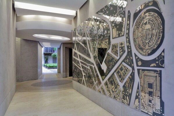 Corredor moderno com um mural da paisagem urbana, iluminação embutida e vista para outra área com plantas.