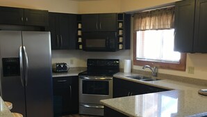 A modern kitchen with dark cabinets, stainless steel appliances, a wooden island, and a window with blinds.
