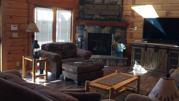 A cozy log cabin interior with a stone fireplace, wooden furniture, and a television.