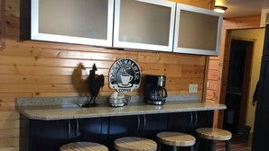 A kitchen with wooden cabinets, a coffee station, and bar stools.