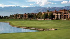 Um campo de golfe com um lago como obstáculo, um clube e montanhas ao fundo.