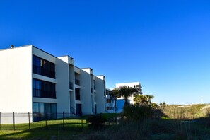 Ein modernes, mehrgeschossiges Gebäude mit Balkonen, einem umzäunten Innenhof und blauem Himmel.
