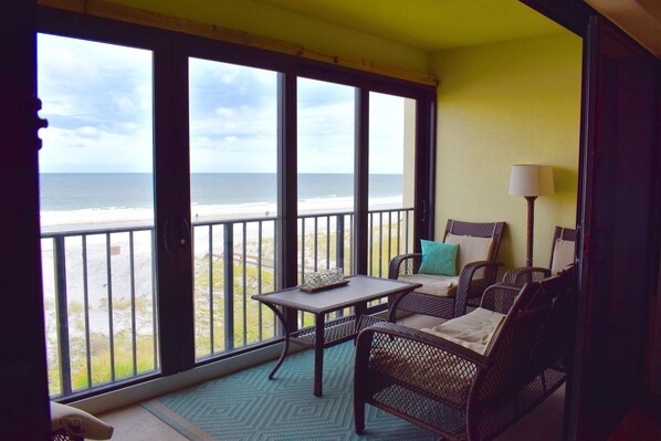 Ein Balkon mit Korbmöbeln, einem Tisch und einer Lampe mit Blick auf einen Strand.
