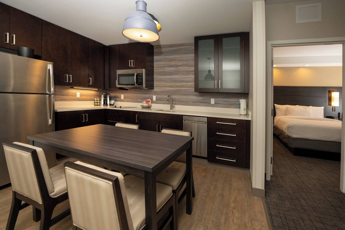 A modern kitchen with dark wood cabinets, stainless steel appliances, and a dining area with a dark wood table and chairs.