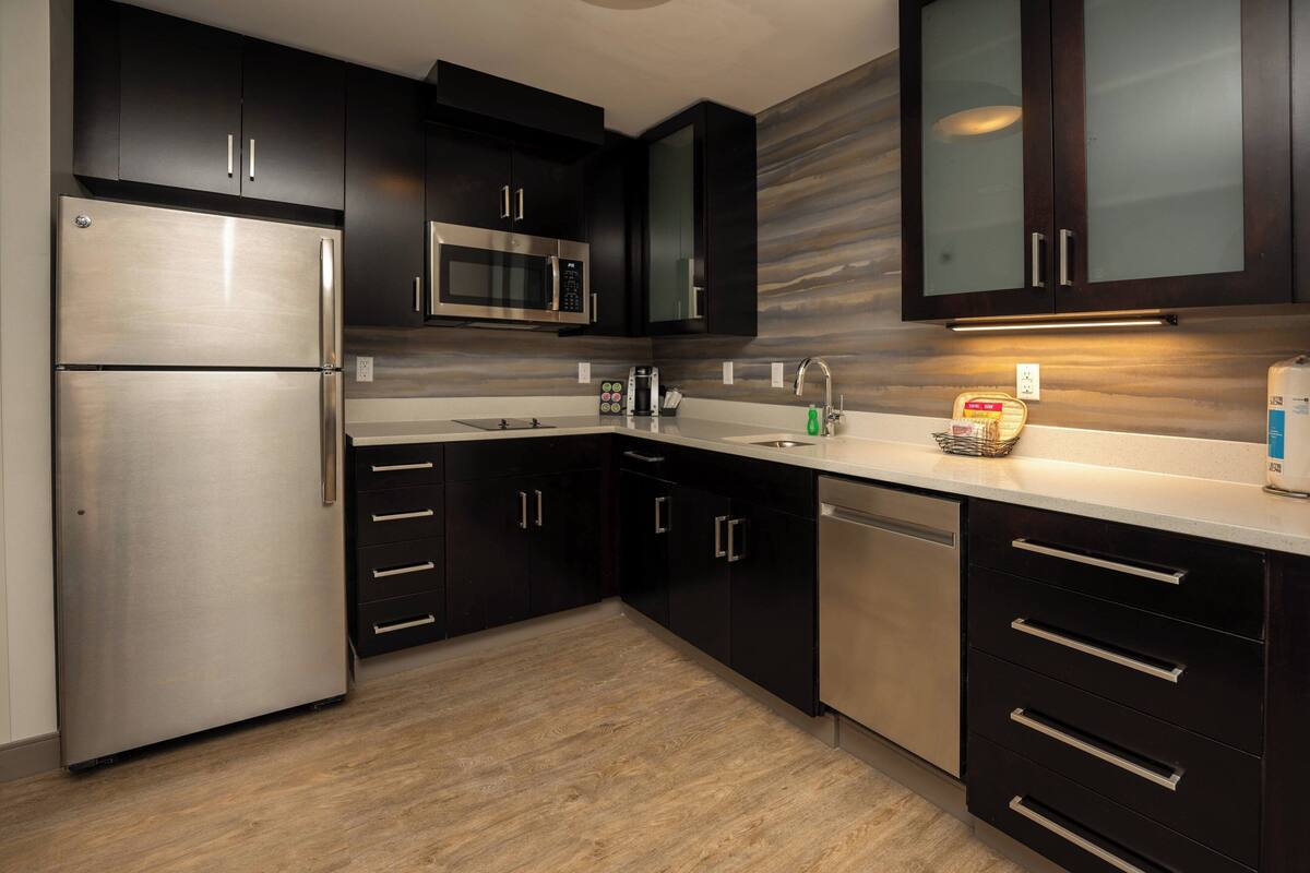 A modern kitchen with dark cabinets, stainless steel appliances, and a light-colored countertop.