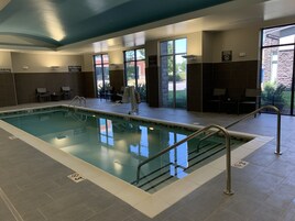 Piscina interior com água cristalina, cadeira de salva-vidas e aviso de ausência de salva-vidas.