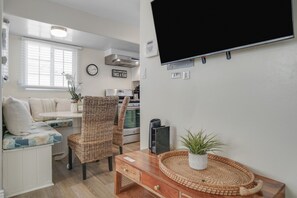 Een knus woongedeelte met een bank, twee stoelen, een televisie, een tafeltje en een kitchenette.