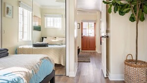 Une chambre à coucher avec un lit, une table de chevet et une fenêtre. Un couloir mène à une porte.