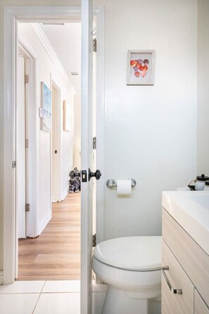 Casa de banho com sanita, rolo de papel higiénico e um quadro na parede.