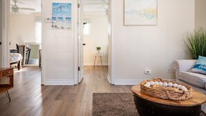 Un salon spacieux doté d’un parquet, d’une table basse agrémentée d’objets décoratifs, d’un canapé avec un coussin et d’un tableau accroché au mur.