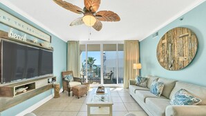 Un salón amplio con una televisión de pantalla plana grande, un ventilador de techo y un balcón con vistas al mar.