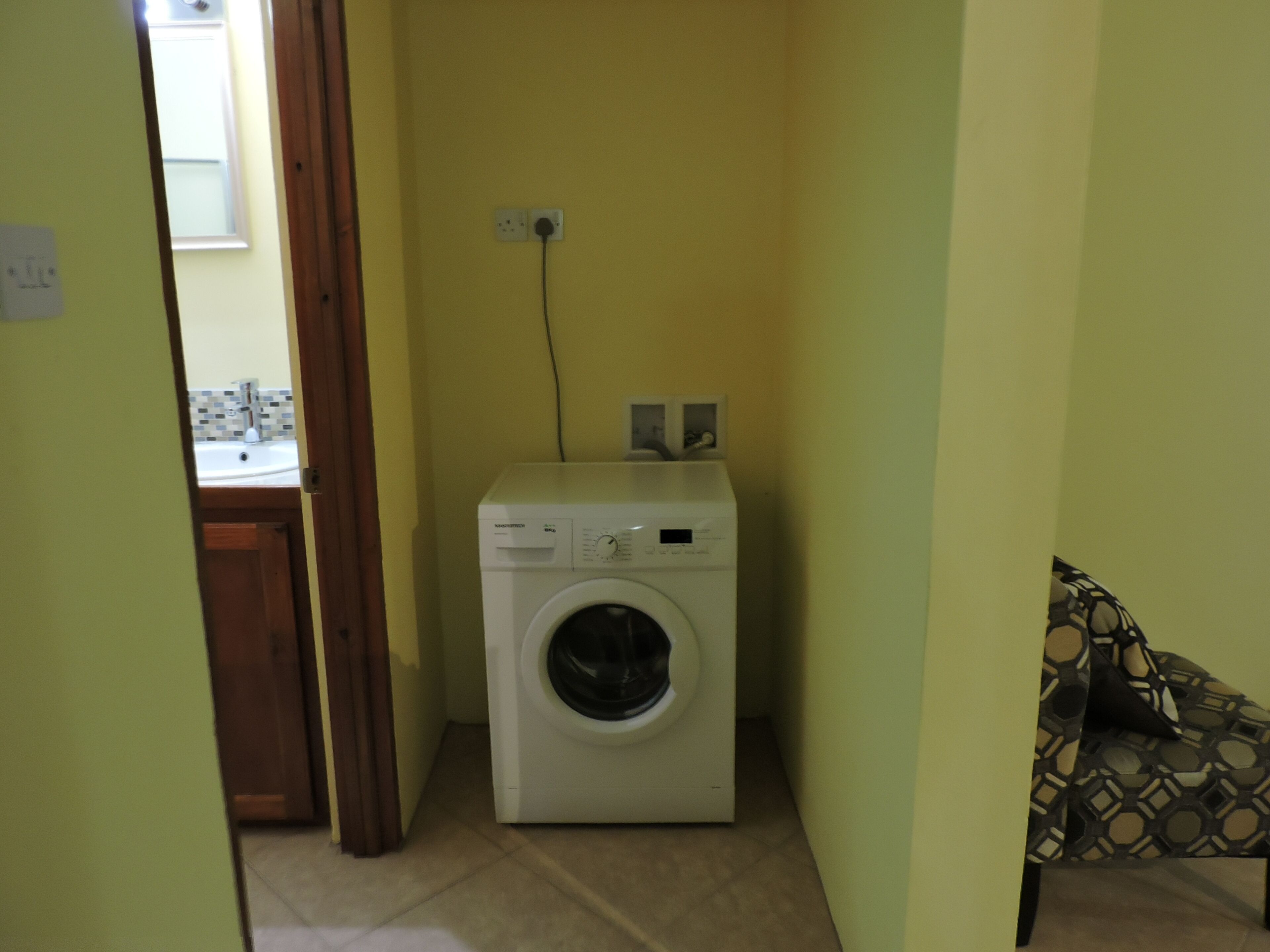 Une petite buanderie comprenant un lave-linge, un petit évier et une prise électrique au mur.