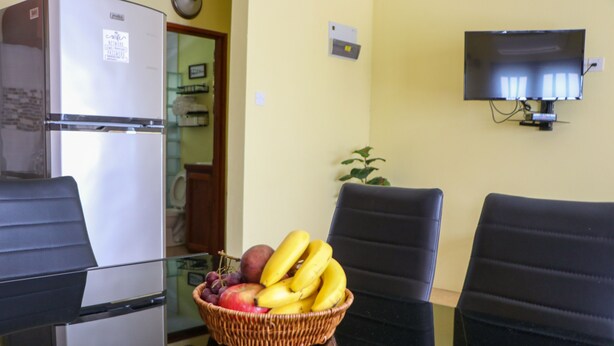 A room with a refrigerator, a television mounted on the wall, and a chair with a basket of fruit on a table. - Cozy one bedroom apartment (Union)