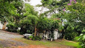 A garden area with a gravel path, white benches, and a small white building with a door. - Village Homestay (Kumphawapi)
