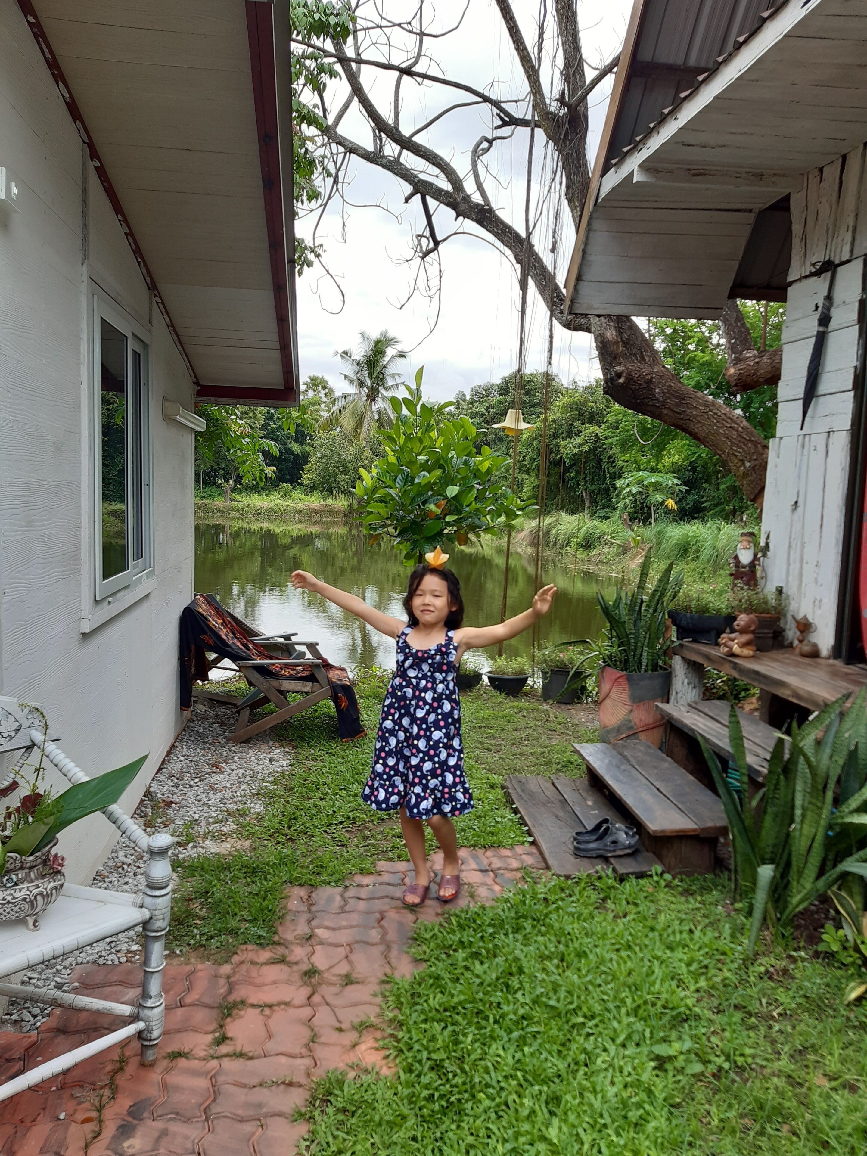 A child standing in a garden with a pond, surrounded by greenery and a wooden bench.