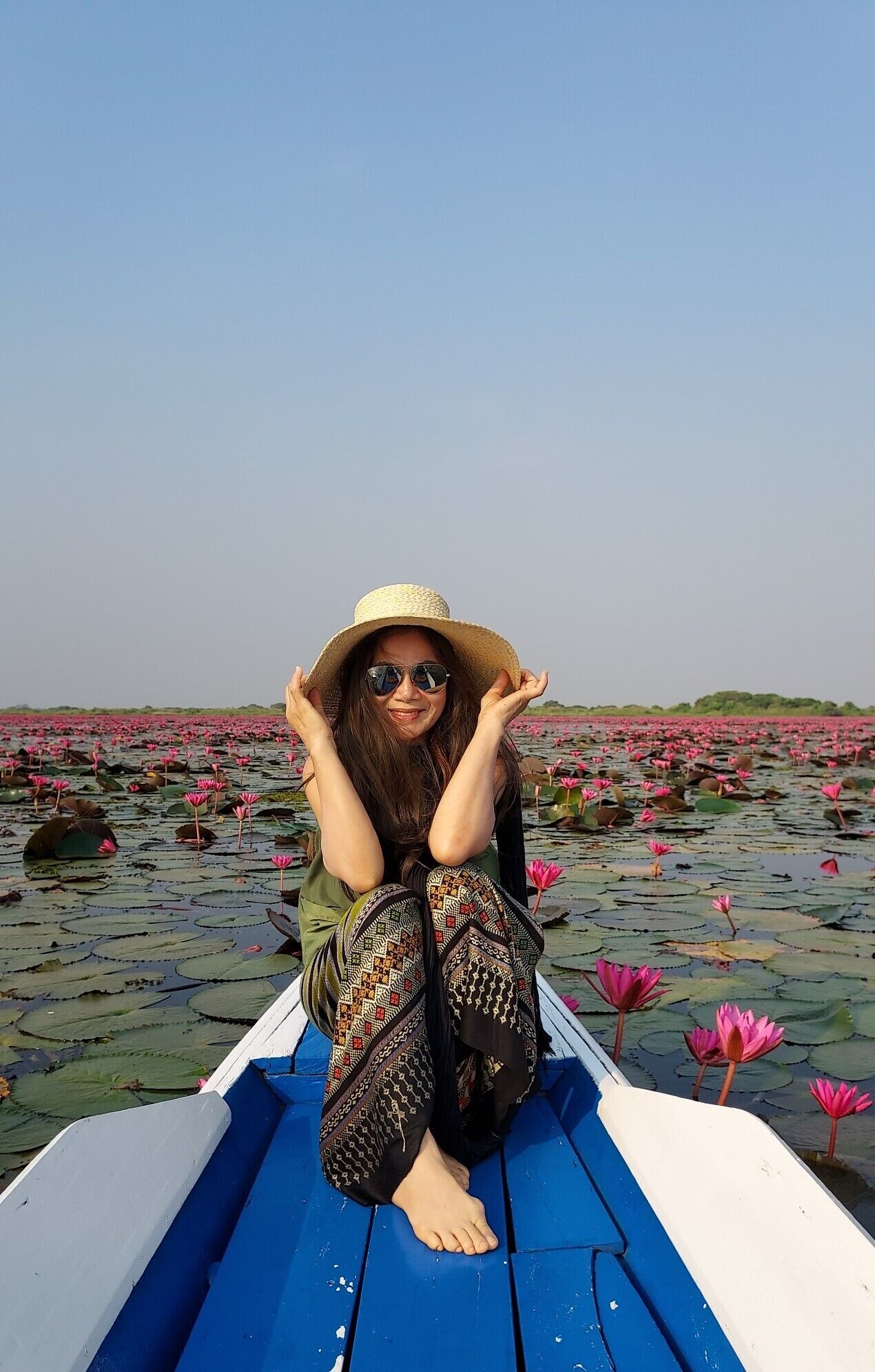 Una persona sentada en un bote, con una extensa superficie de agua y flores de loto al fondo.